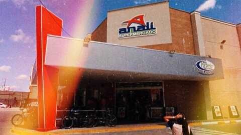 Foto de uma entrada frontal do mercado Anali. Acima da entrada a um logo com a letra 'A' destacada na cor vermelha com o nome completo logo abaixo na cor azul.